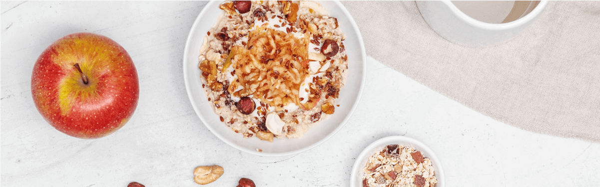 Bircher Müsli in der Schüssel mit Nüssen dekoriert und einem Apfel daneben