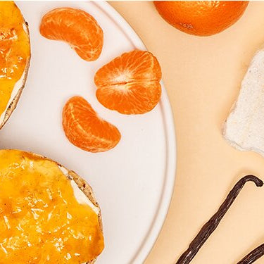 Zwei Scheiben Brot mit Mandarinen Marmelade auf einem Teller undMandarinen Marmelade mit Mandarinen daneben