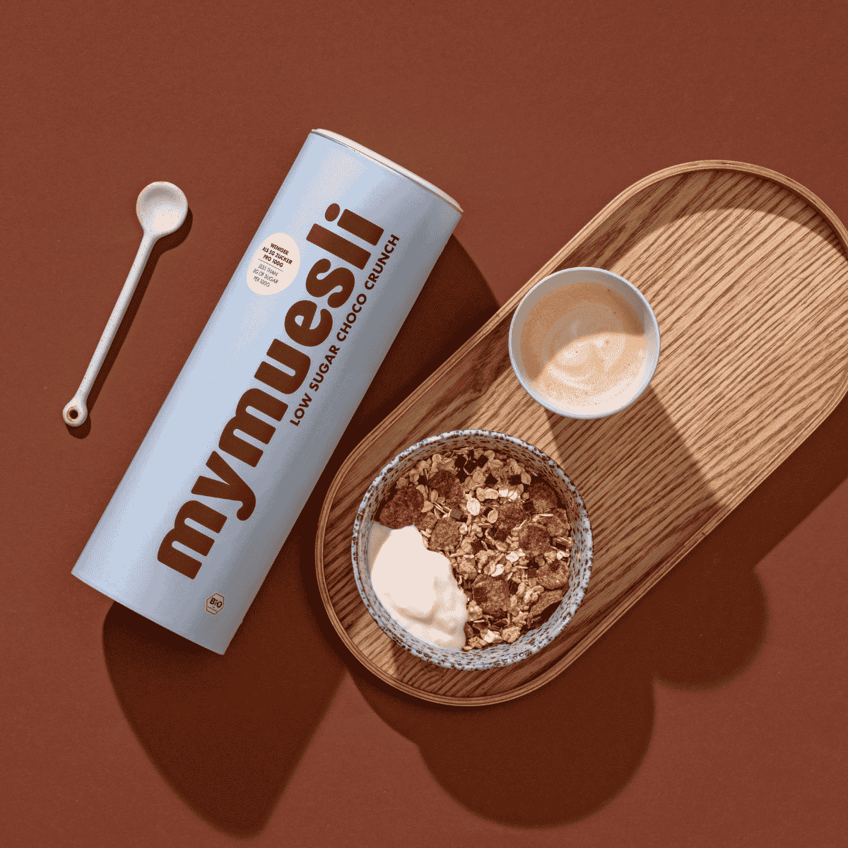 Das mymuesli Low Sugar Choco Crunch Müsli angerichtet mit frischem Joghurt auf einem Holz Brett als Teil des Feel Good Bundles