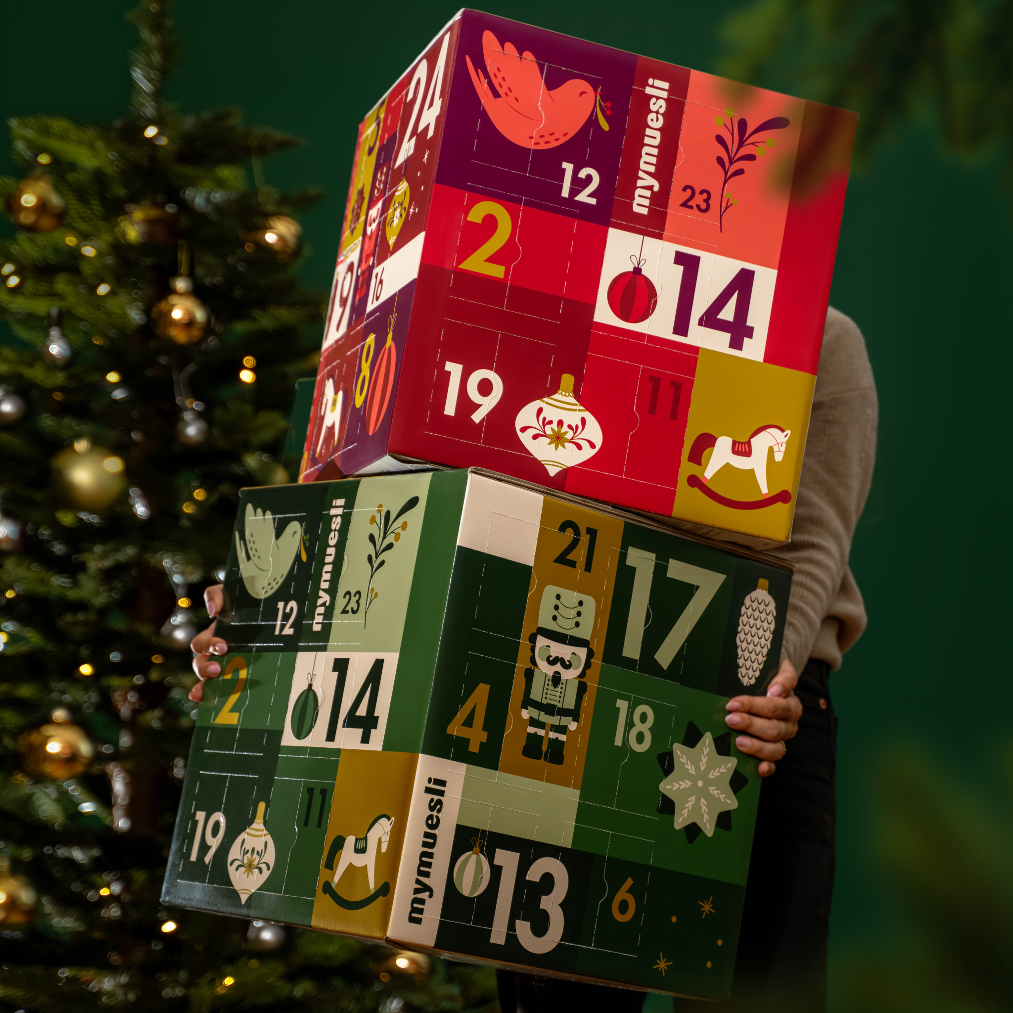 mymuesli Bio Müsli und Porridge Adventskalender, getragen von einer Frau in weihnachtlich grünem Hintergrund.