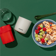 mymuesli Apfelreibe neben Schale mit Bio Bircher Müsli mit frischen Himbeeren, Blaubeeren und Trauben