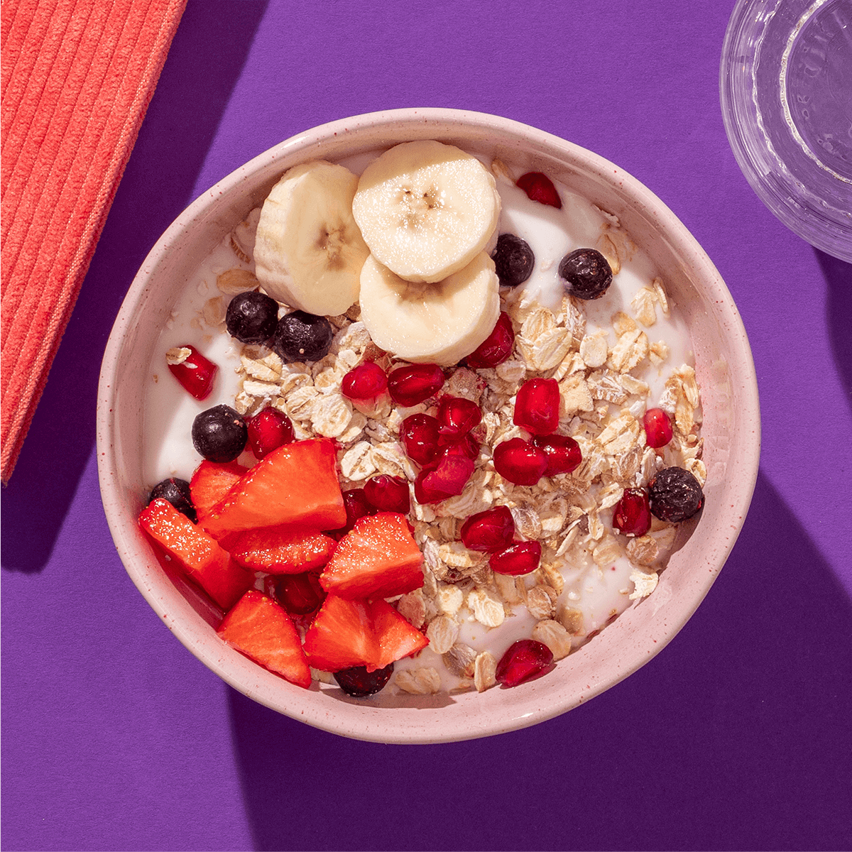 mymuesli Bio Fit in Shape Superfruit Müsli in Schale mit Milch sowie frischen Bananen, Erdbeeren und Granatapfelkernen