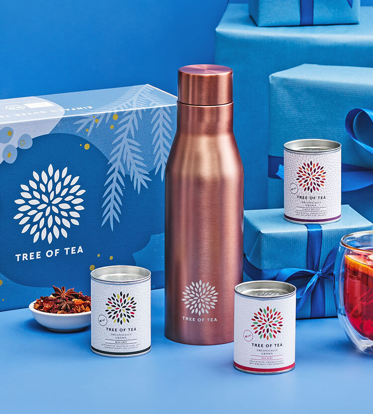 Tree of Tea Infuser Teeflasche in Rosegold und kleine Teedosen vor festlichem Hintergrund
